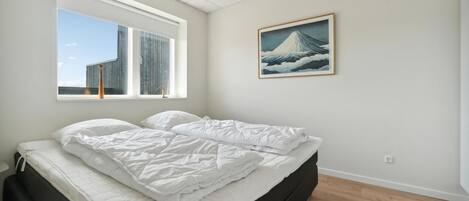 A bedroom with a bed, a window with a view of buildings, and a painting on the wall.