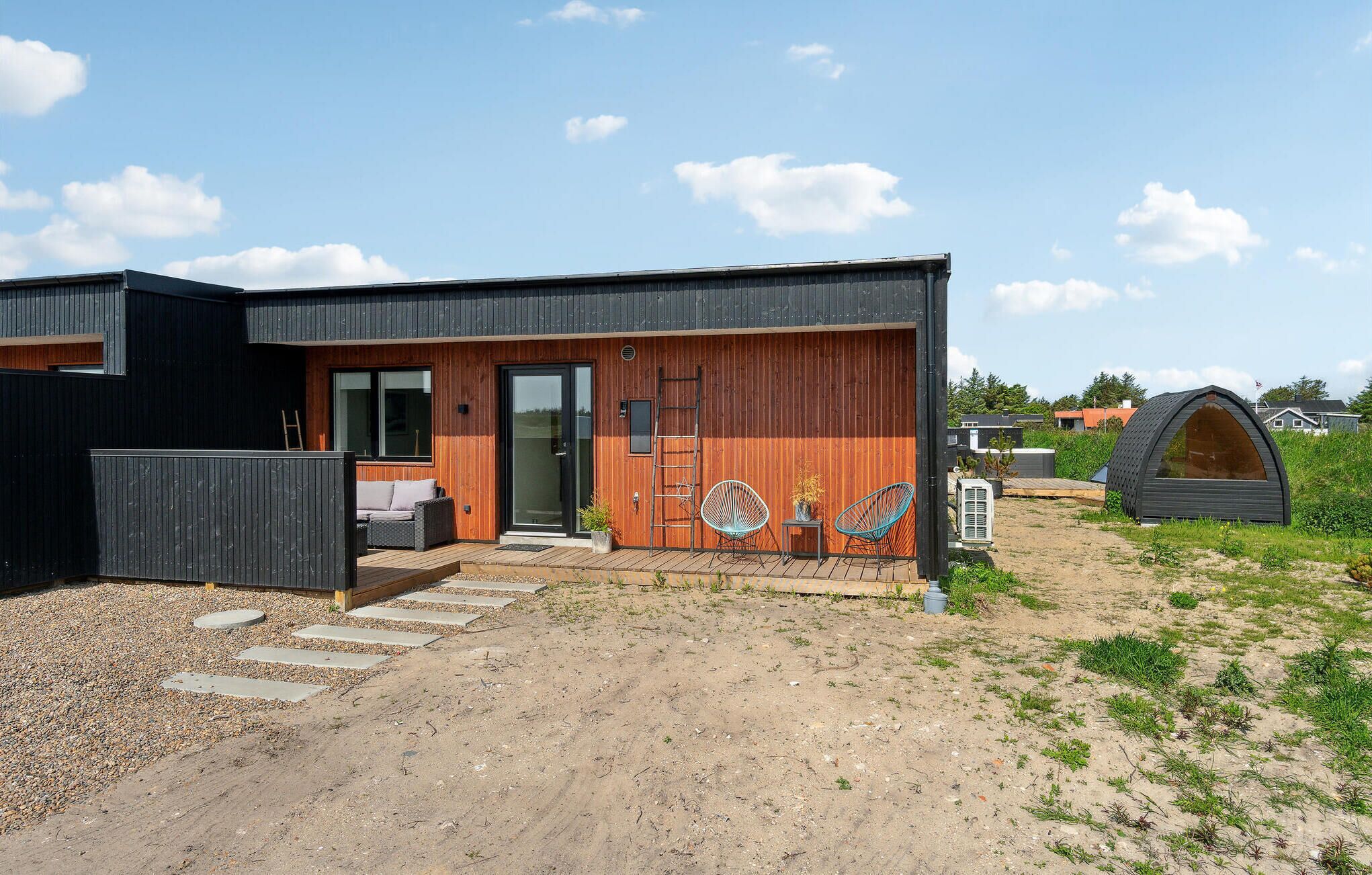 A modern house with a wooden exterior, a porch with outdoor seating, and a small garden area.