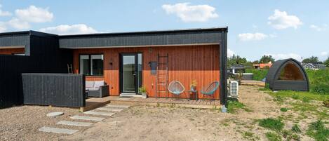 A modern house with a wooden exterior, a porch with outdoor seating, and a small garden area.