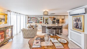 A modern living room with a zebra-patterned sofa, a coffee table with books and glasses, a kitchen with a dining area, and a large bookshelf. - Luxurious home in Grimaud (Grimaud)