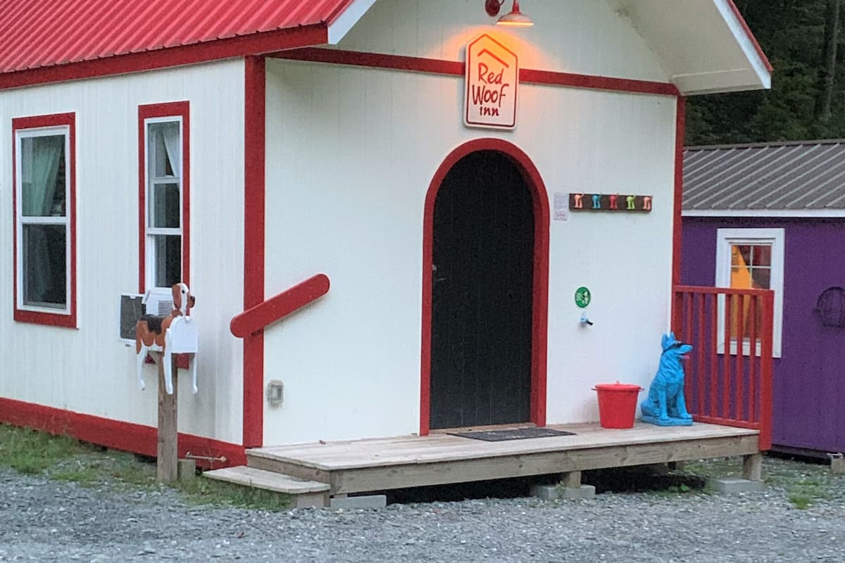 Pieni, yhden kerroksen rakennus, jossa on punainen katto ja valkoiset seinät. Rakennuksen kyltissä lukee ”Red Woof Inn”. Siinä on puinen kuisti, postilaatikko ja pieni patsas.
