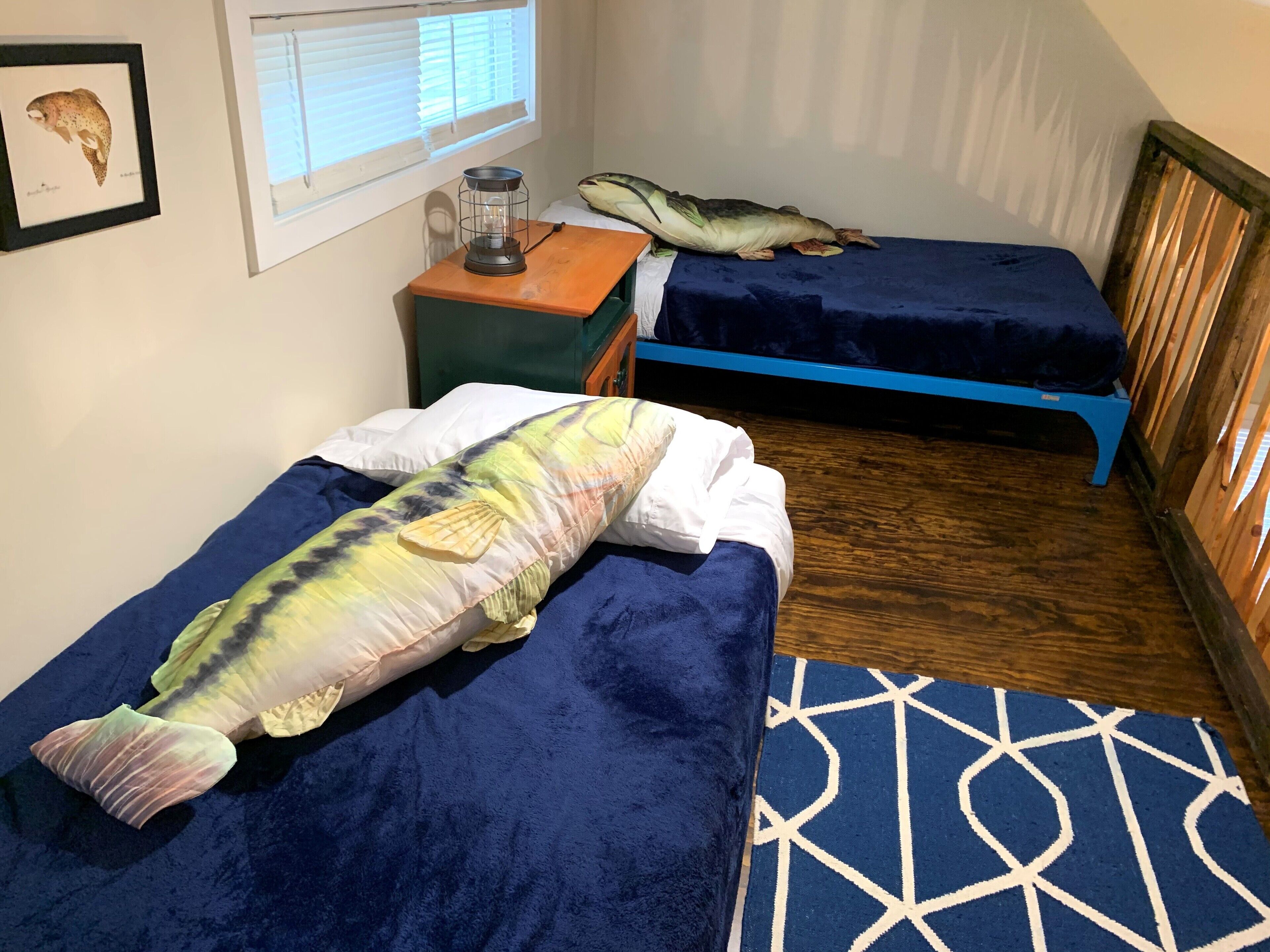 A room with two beds, one with a fish-shaped pillow and another with a pillow shaped like a fish.