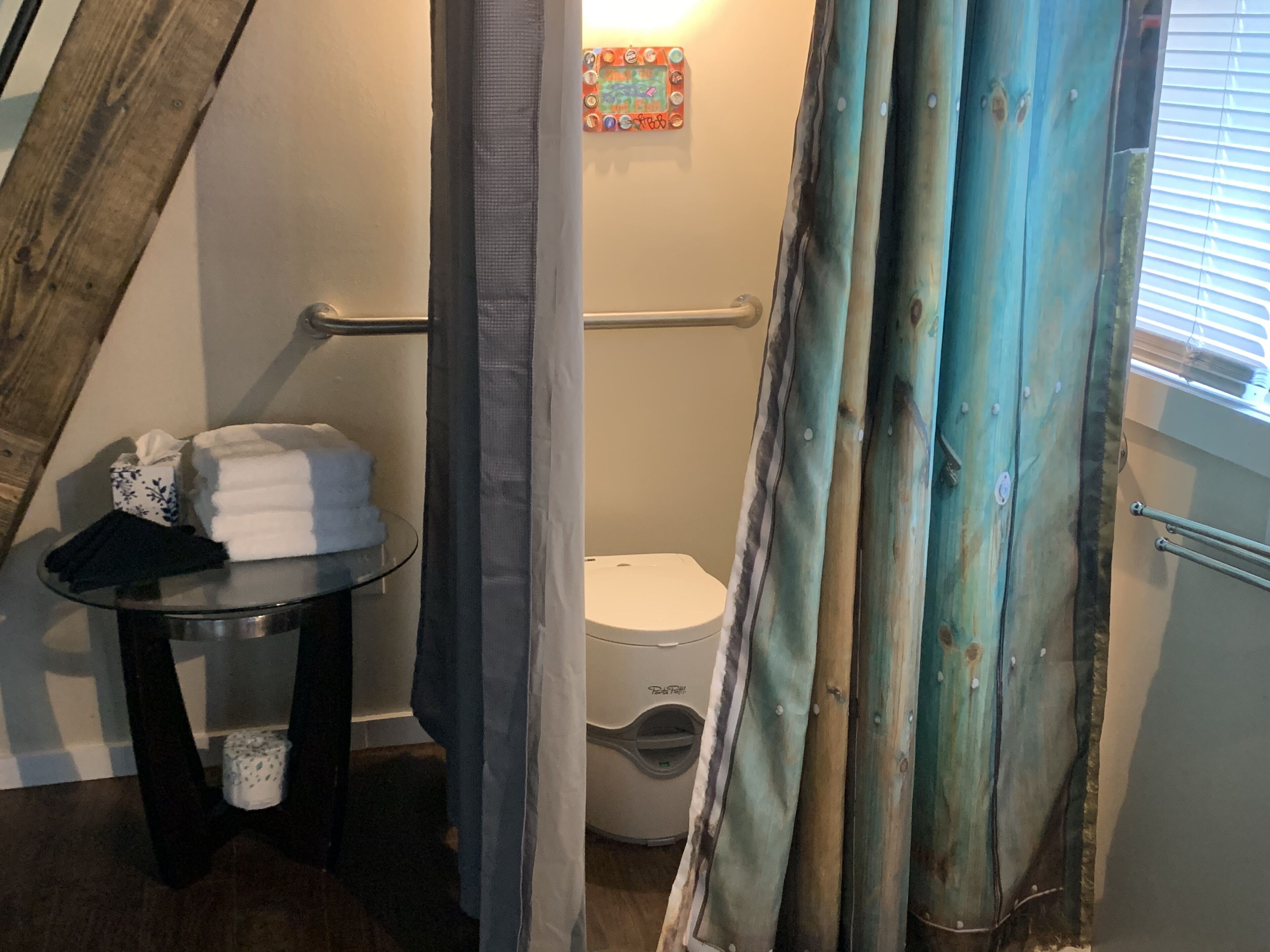 Un baño con inodoro, una mesa de vidrio y toallas, y cortina de ducha.