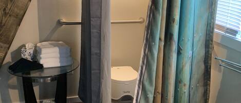 Un baño con inodoro, una mesa de vidrio y toallas, y cortina de ducha.