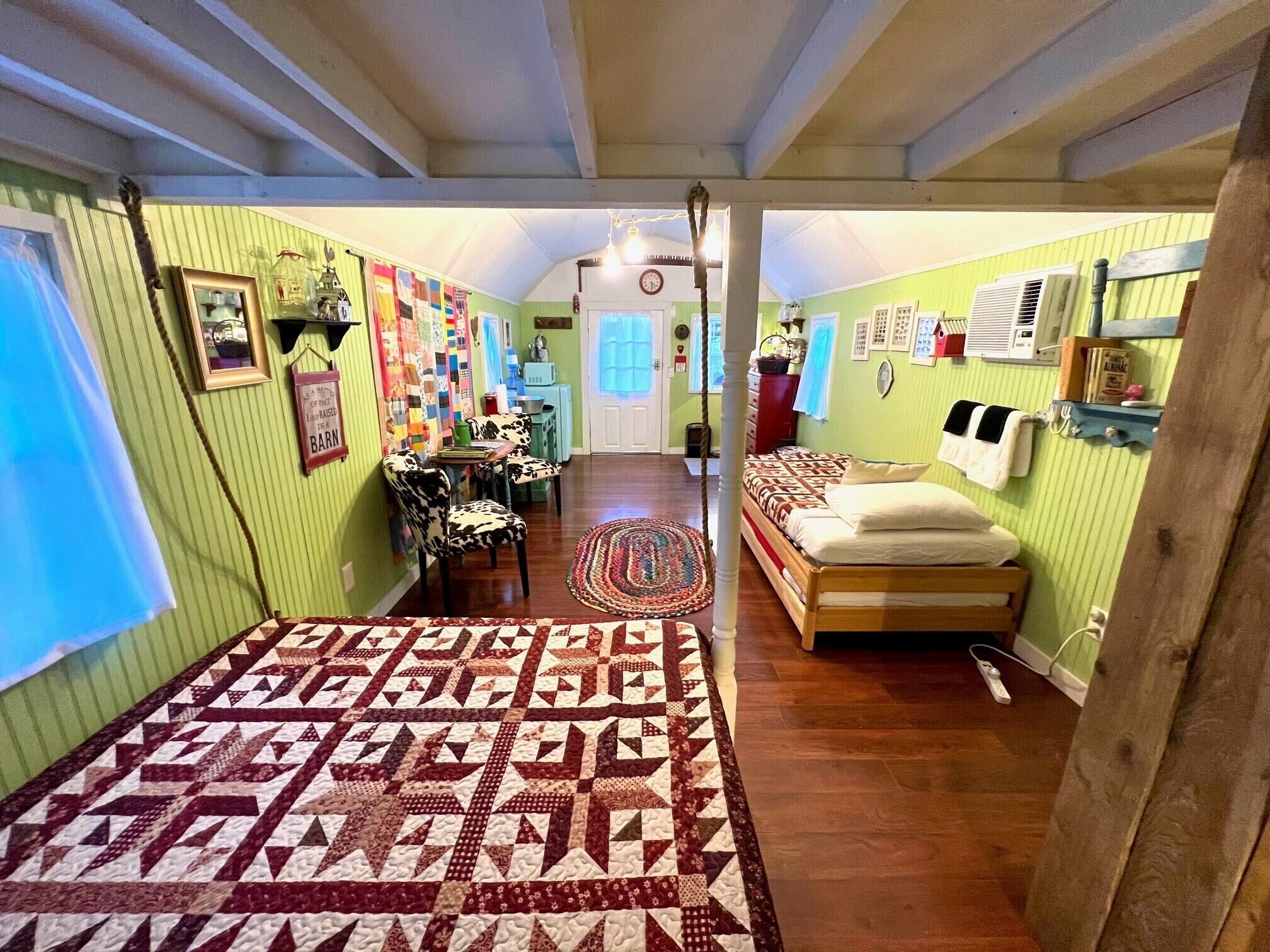 A cozy, well-lit hallway with a wooden floor, a patterned rug, and a bed with a quilt.