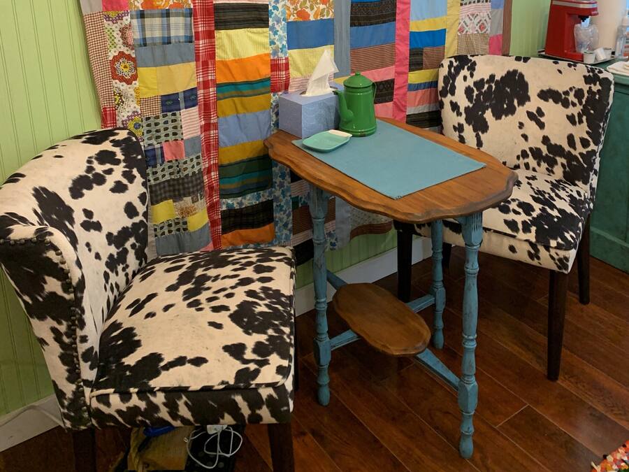 Un pequeño comedor con una mesa de madera y dos sillas con estampado de cuero. Hay una caja de pañuelos y una cafetera verde sobre la mesa.