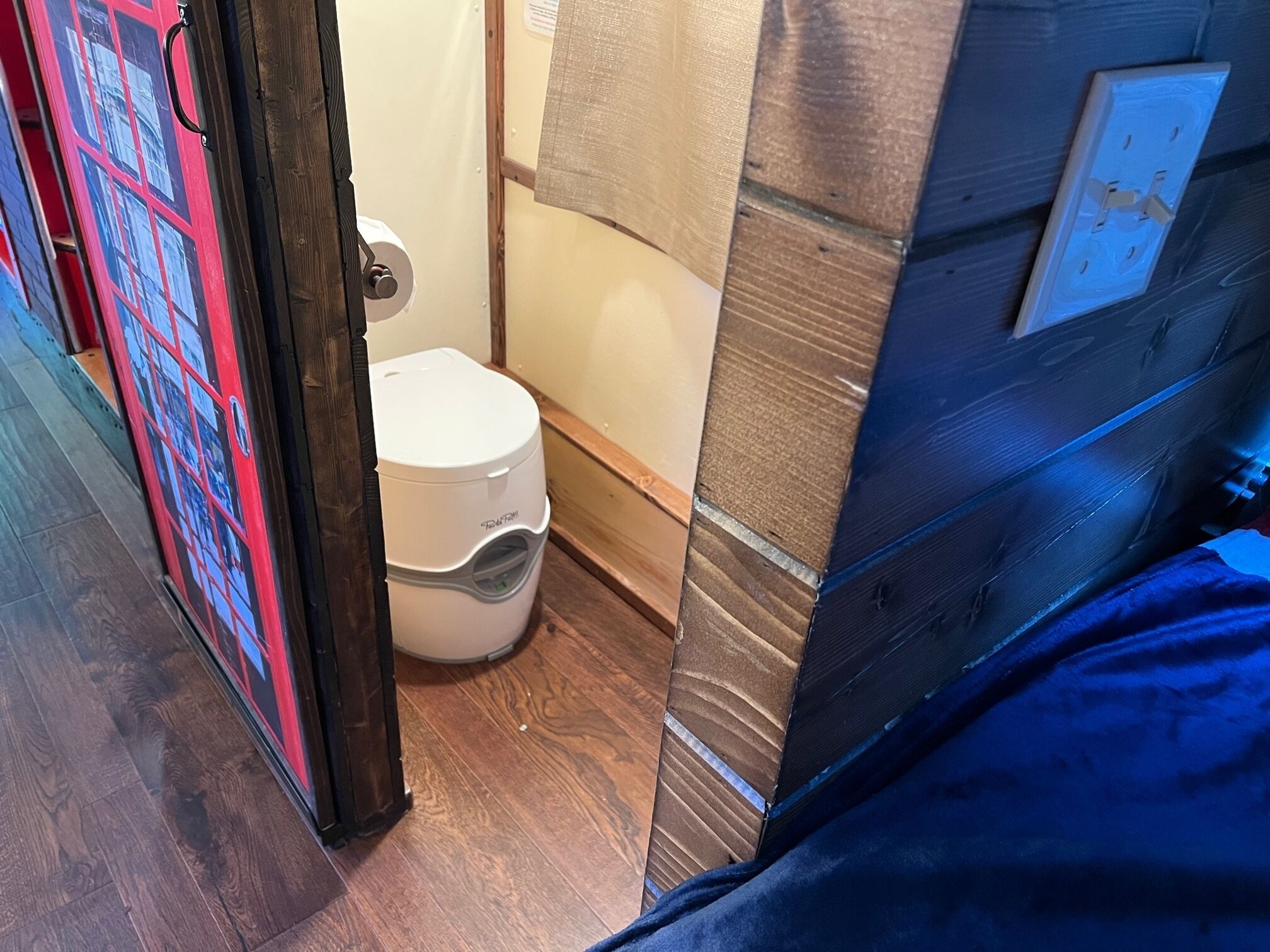 A small bathroom with a toilet, a wooden floor, and a blue wall.