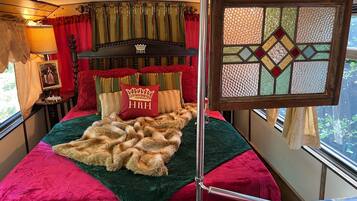 Ein Schlafzimmer mit einem Bett, einem Kopfteil mit einem Kronenwappen, einem roten Kopfkissen mit dem Schriftzug "HRH" und einem Fenster mit geometrischem Muster.