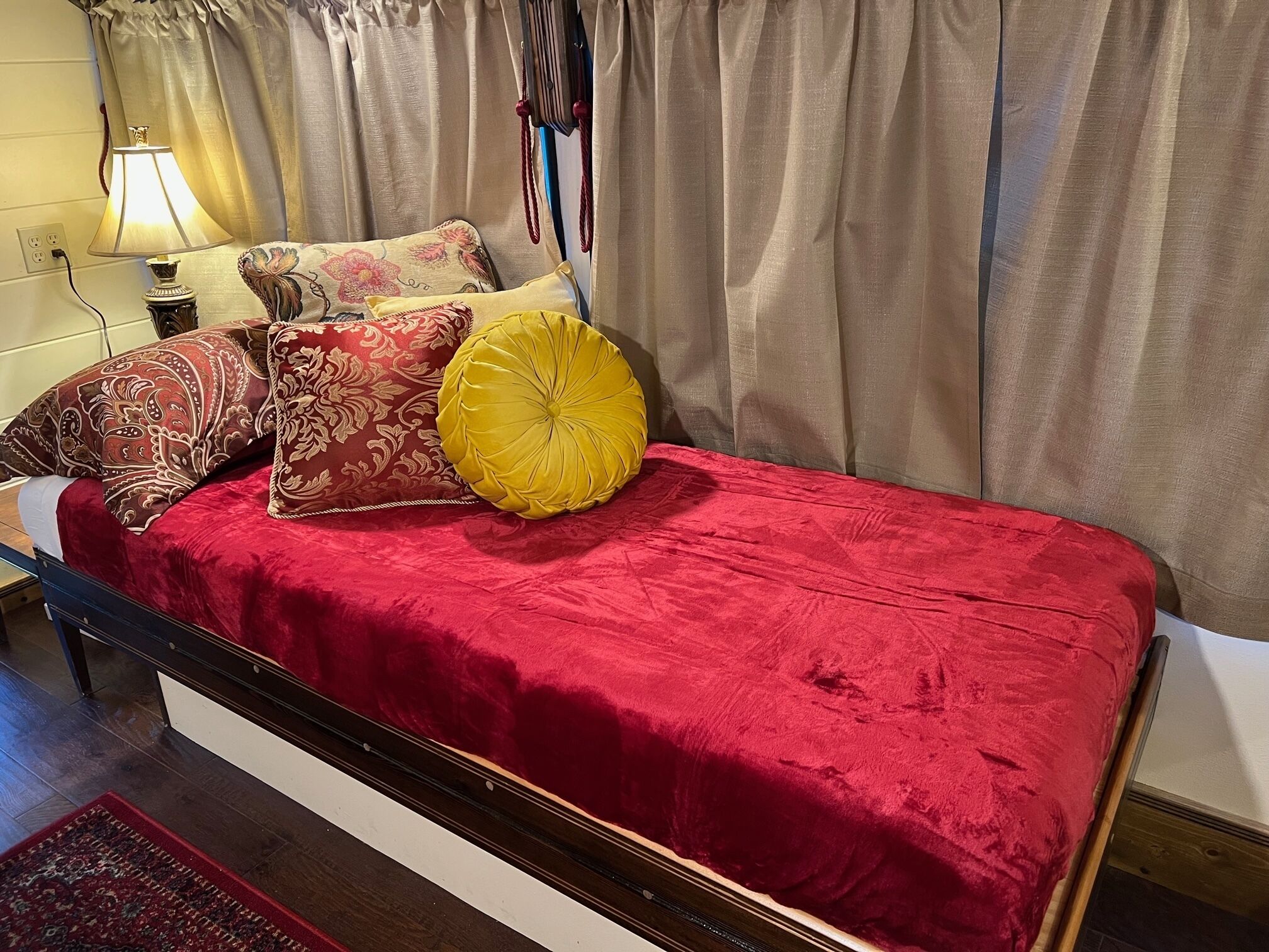 Una cama con una colcha de terciopelo rojo, un cojín decorativo amarillo y cojines estampados.
