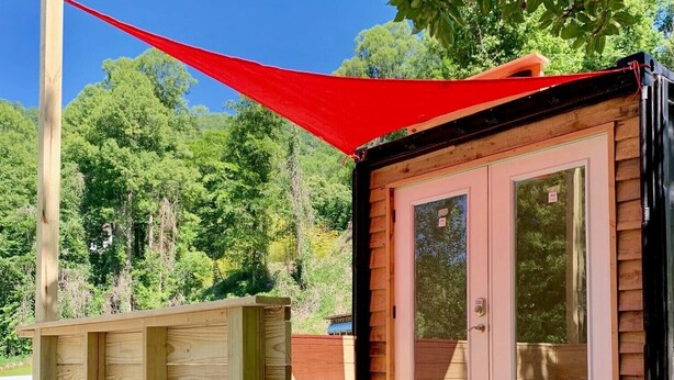 A small wooden cabin with a deck and a red canopy.