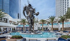 A pool area with a central sculpture, surrounded by palm trees and modern buildings. - Palms Place Vacation Suites Collection (Las Vegas)
