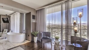 Una habitación de hotel moderna con un ventanal grande, una bañera y una zona de estar con vistas a la ciudad.