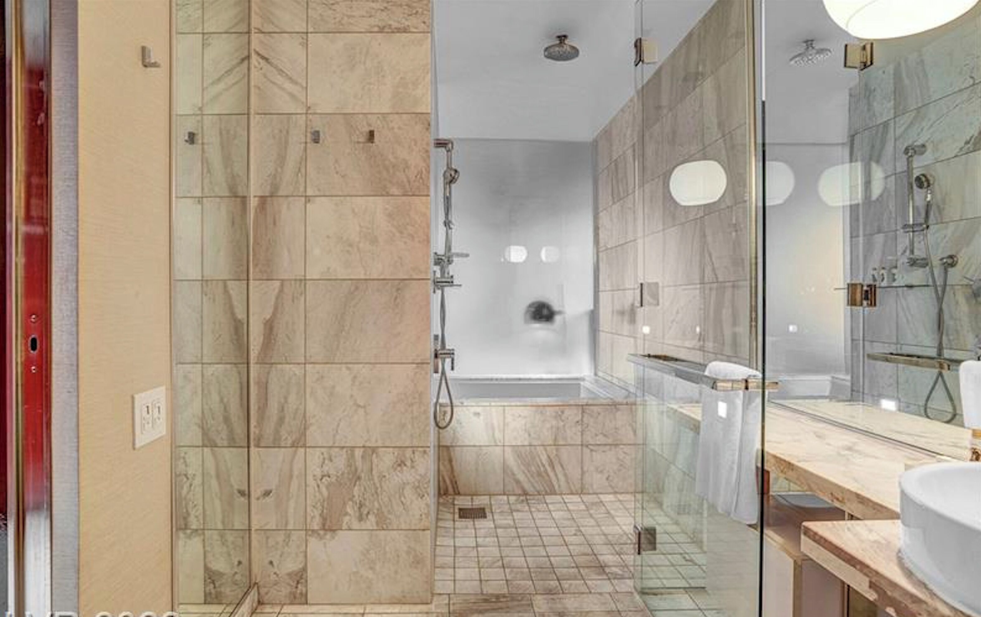 Ein modernes Badezimmer mit einer Glaskabine zur Dusche, Marmorfliesen und einem großen Spiegel.