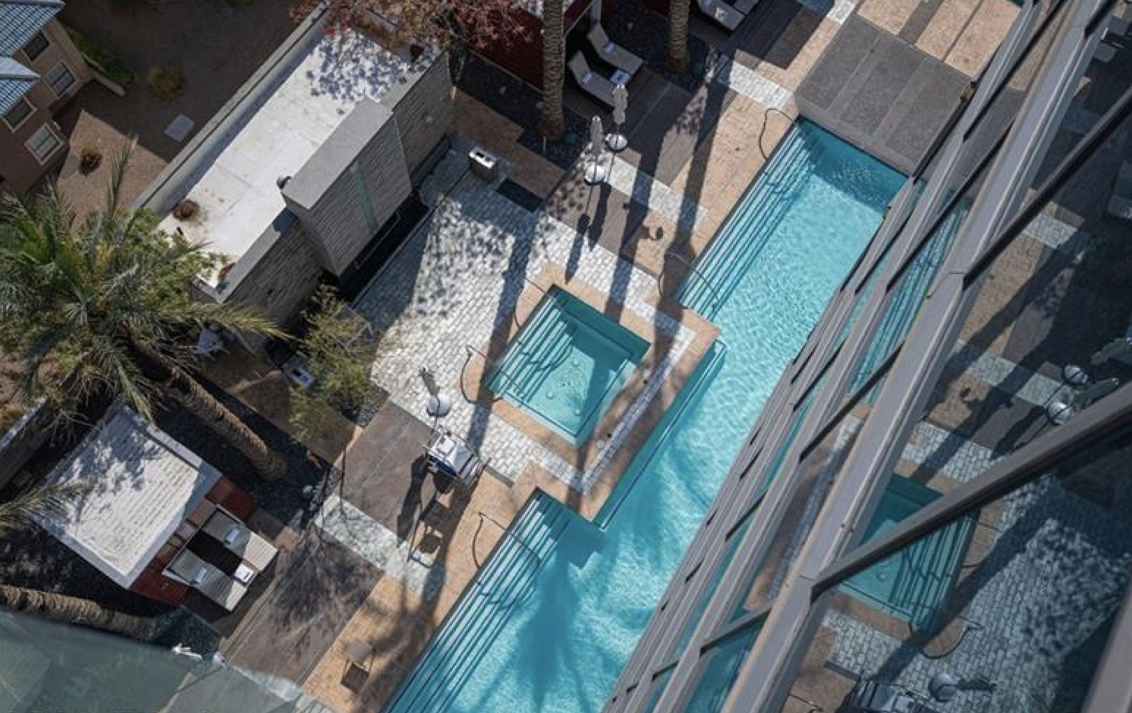Vue aérienne d’un hôtel doté de plusieurs piscines, de palmiers et d’une terrasse carrelée.