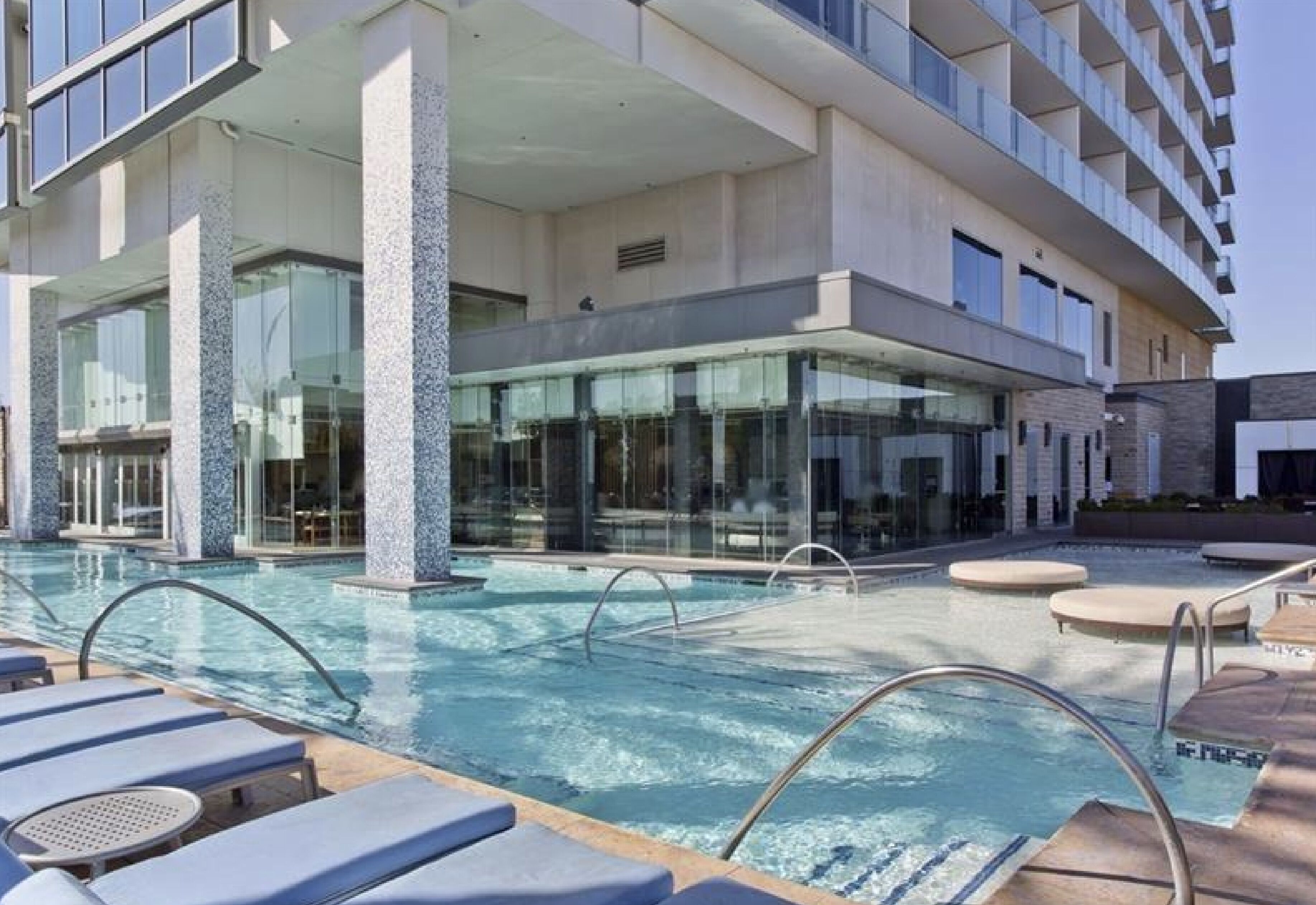 Een modern hotel met een zwembad, ligbedden en een wellnessruimte met glazen wanden.