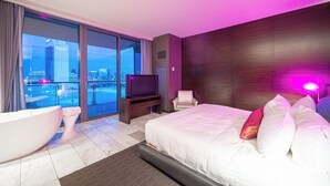 Una habitación de hotel moderna con una cama grande, una bañera, un televisor y vistas a la ciudad.