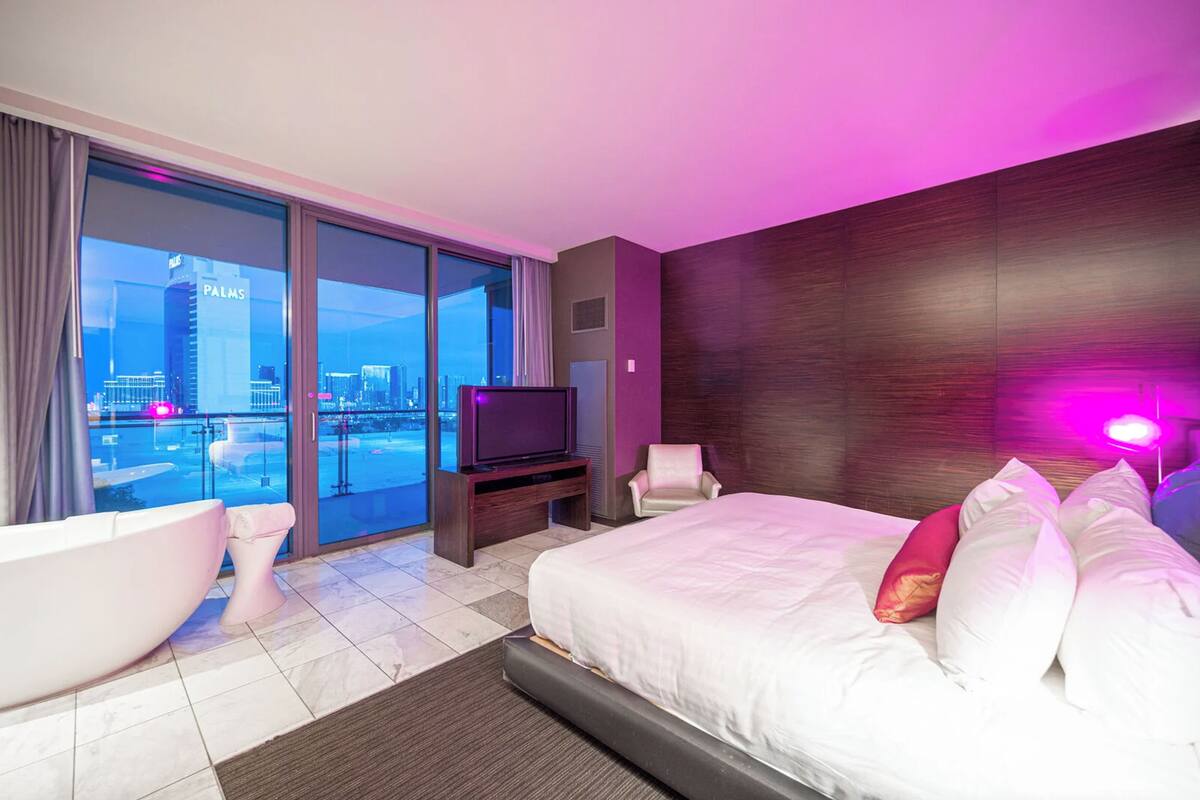 Een moderne hotelkamer met een groot bed, een badkuip, een televisie en uitzicht over de stad.