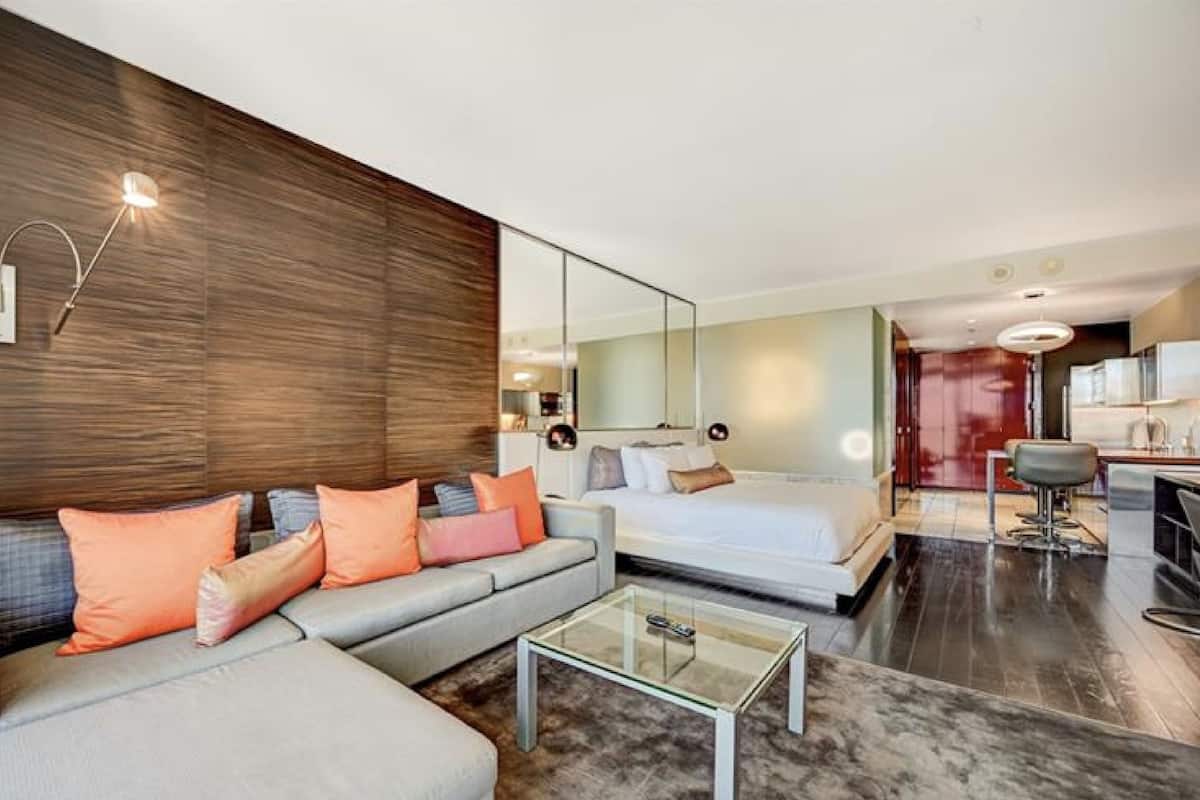 Een moderne hotelkamer met een bank, een glazen bijzettafeltje, een bed en een kitchenette.