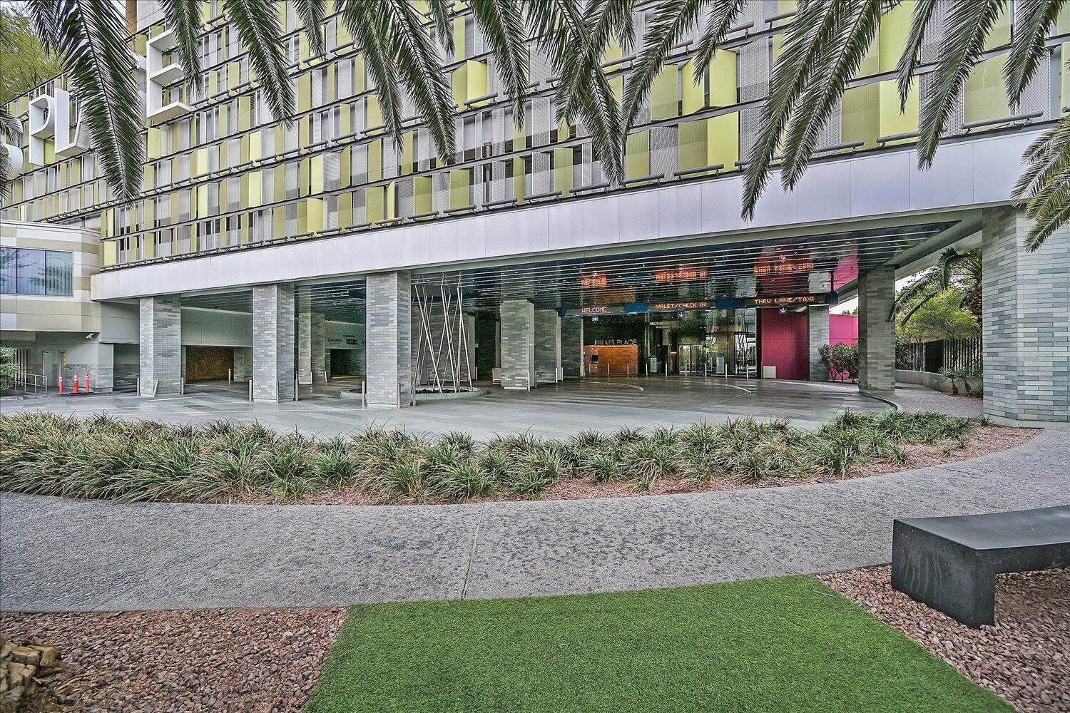 Un bâtiment moderne doté d’un porche, de rampes en verre et de palmiers.