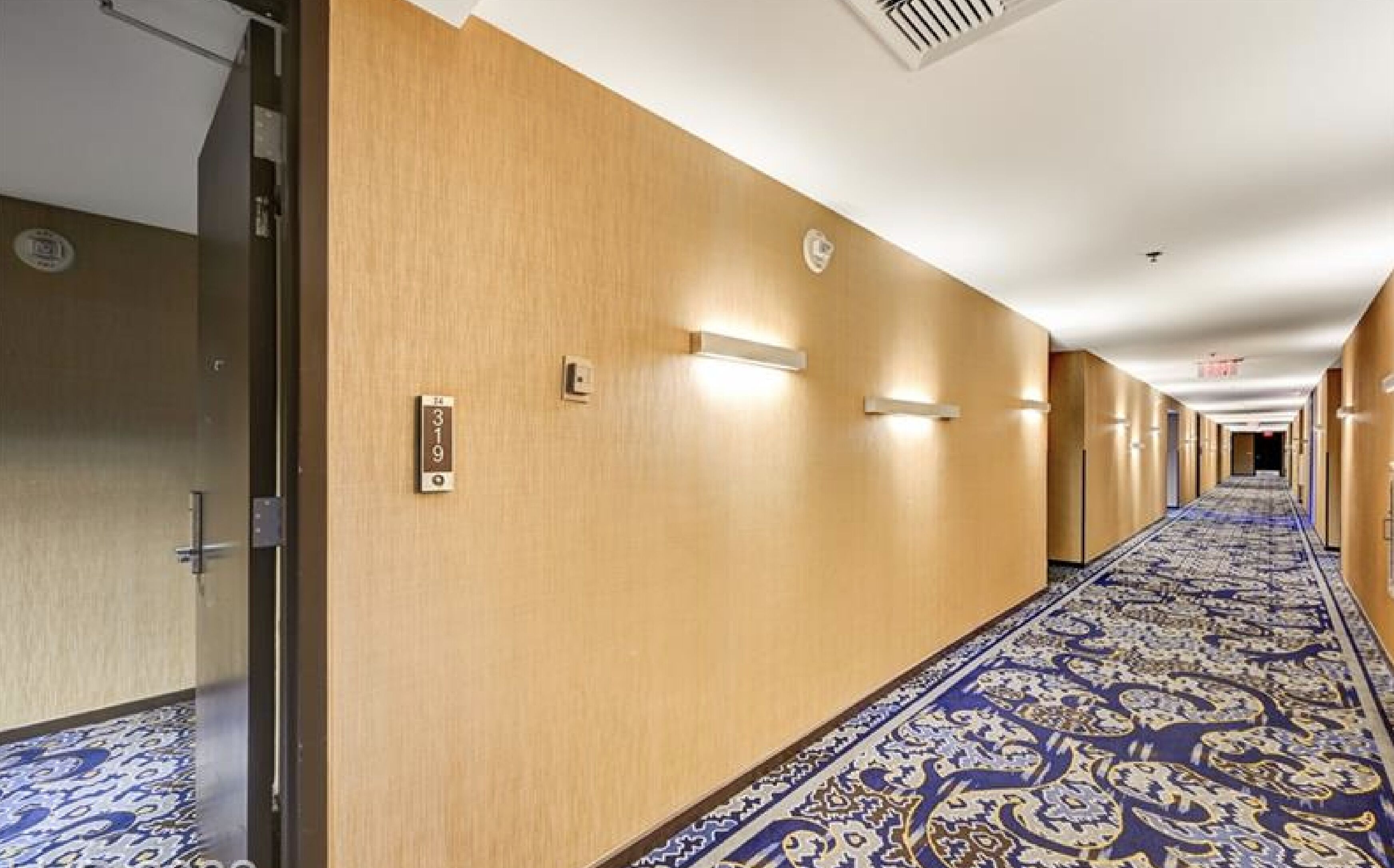 En hotellkorridor med träpanel på väggarna, numrerade dörrar och ett mönstrat golv.