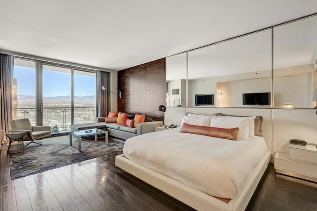 Een moderne hotelkamer met een groot bed, een bank, een bijzettafeltje en uitzicht op de stad.