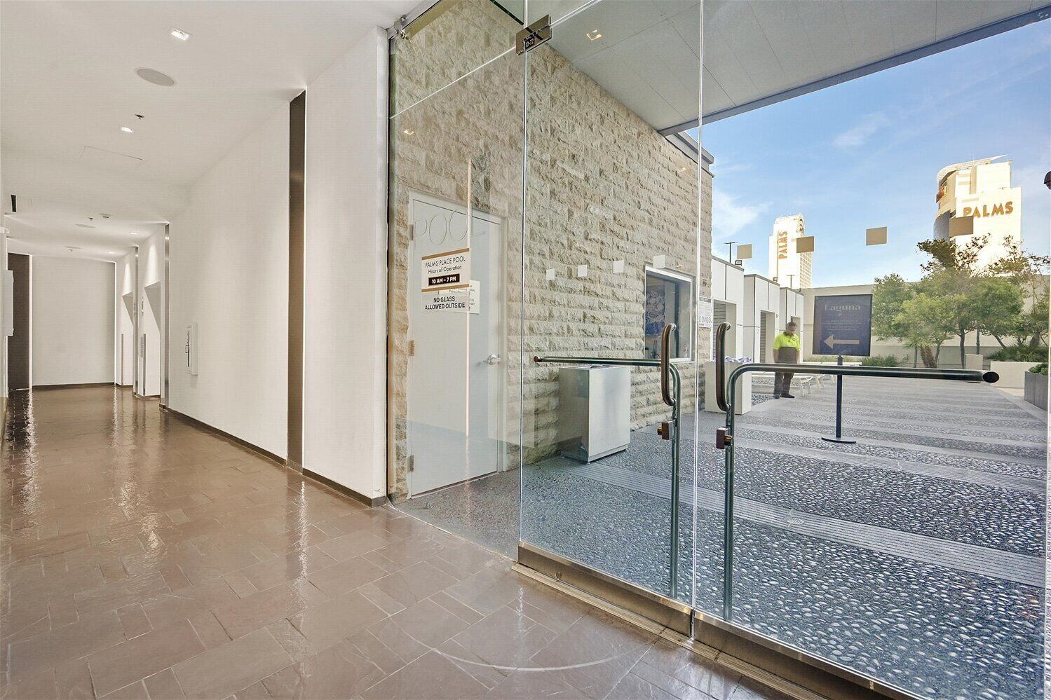 Un hall d’hôtel moderne avec une entrée dotée d’une porte en verre, un mur en pierre et un panneau indiquant l’emplacement de la piscine.