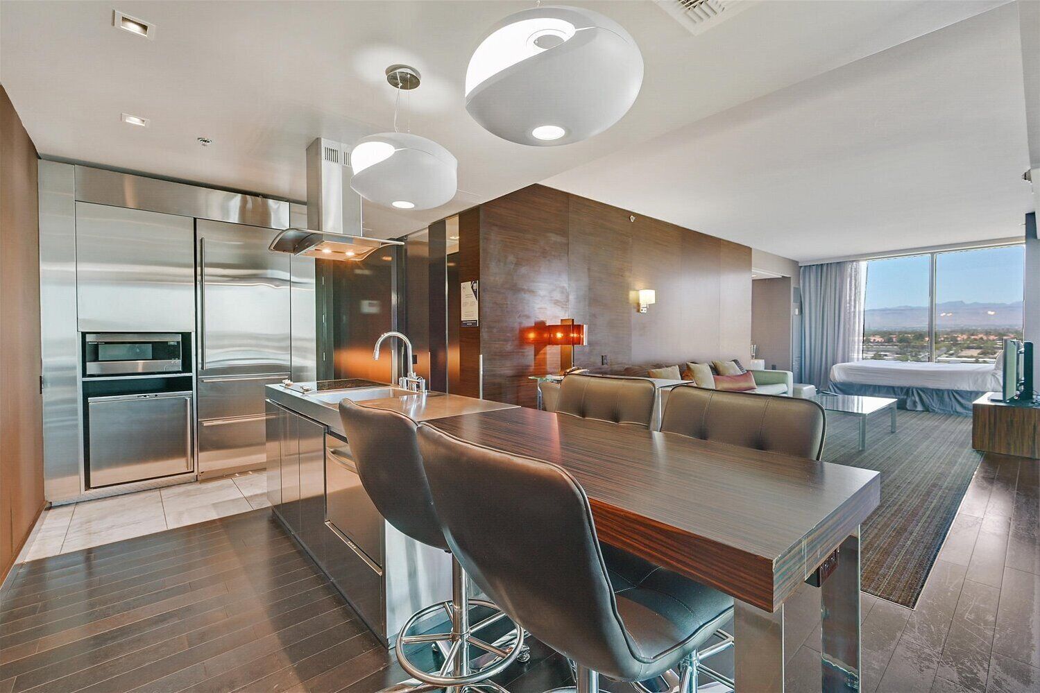 A modern kitchen with stainless steel appliances, a central island with bar stools, and a dining area with a large window offering a city view.