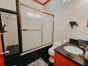 Un baño con un espejo grande, inodoro, lavamanos y zona de ducha.