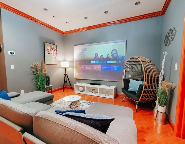 Una sala de estar moderna con un televisor de pantalla plana grande, asientos cómodos, una lámpara de pie y plantas decorativas.
