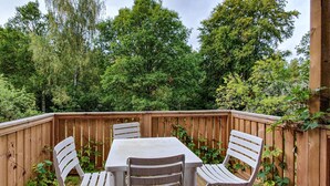 A wooden deck with a table and four chairs, surrounded by a wooden fence and lush greenery. - Beautiful home in älmhult with kitchen (Älmhult)