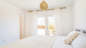 Une chambre avec un grand lit, des rideaux blancs et une vue sur l’extérieur.
