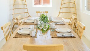 Une table à manger dressée pour quatre personnes, avec des chaises en osier, une plante en pot et de la verrerie transparente.