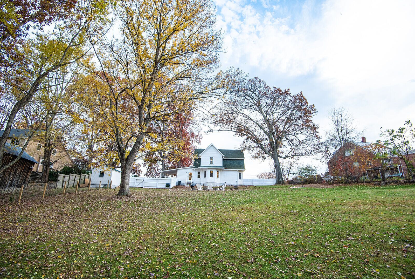 A white house with a green roof, surrounded by a grassy yard and trees with autumn leaves.
