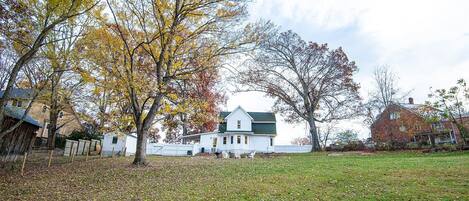 A white house with a green roof, surrounded by a grassy yard and trees with autumn leaves.