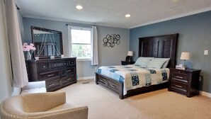 Quarto com cama, cômoda, cadeira e mesas de cabeceira.