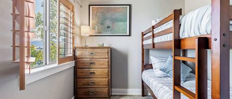 Un dormitorio con dos camas literas de madera, un aparador con cajones, una ventana con persianas y un cuadro en la pared.