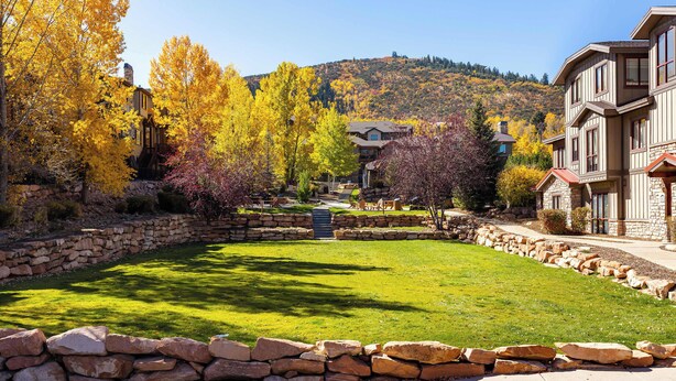 A residential area with stone walls, a well-maintained lawn, and autumn-colored trees. - Bear Hollow Heaven Private Hot Tub 4 Bedroom Luxury Condo (Park City)