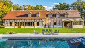 Een groot huis met een zwembad, een terras met stoelen en een overdekt buitengebied.