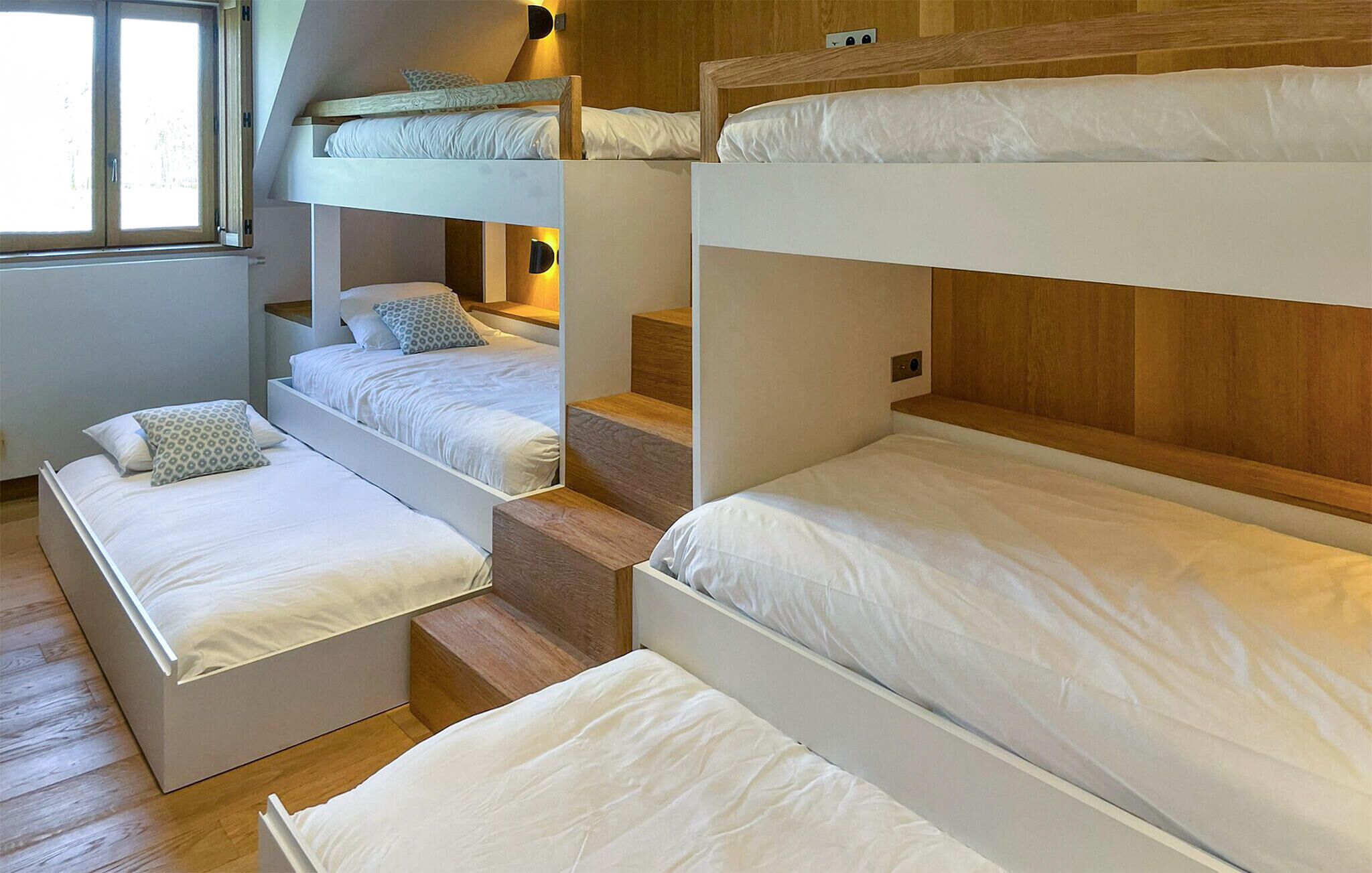 Een slaapzaal met stapelbedden, een trap en een raam.