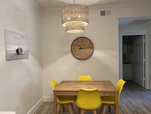 Un'area pranzo con un tavolo di legno e sedie gialle, una sveglia a parete e un lampadario.