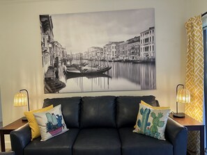 Un divano in pelle nera con due cuscini decorativi, un grande dipinto di una città in bianco e nero e due lampade da tavolo su entrambi i lati.