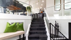 Un intérieur moderne avec un escalier, un banc doté de coussins verts et un coin cuisine.
