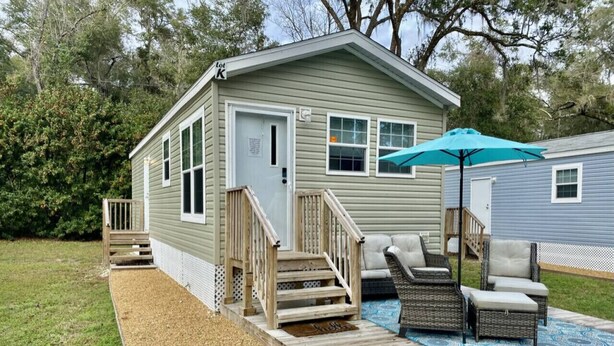 A small, single-story cabin with a deck, outdoor seating, and a covered patio area. - Rainbow River Bungalow K (Dunnellon)