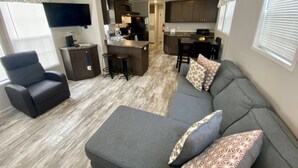 A modern living room with a gray sectional sofa, a black armchair, and a flat-screen TV mounted on the wall. - Rainbow River Bungalow K (Dunnellon)