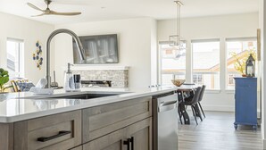 A modern kitchen with a large island, stainless steel appliances, and a dining area with a blue cabinet and chairs. - Modern Happy Valley Executive TH with Hot Tub (Beaverdell)