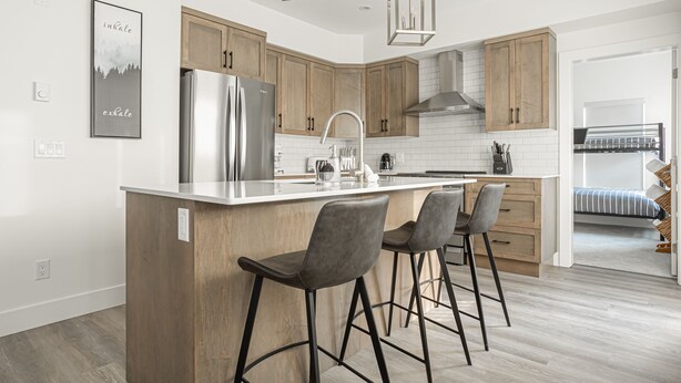 A modern kitchen with wooden cabinets, a stainless steel refrigerator, and a bar area with stools. - Modern Happy Valley Executive TH with Hot Tub (Beaverdell)