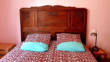 A bed with a patterned bedspread and two pillows, a wooden headboard, a bedside table, and a floor lamp.