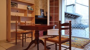 A dining area with a round wooden table, two chairs, a bookshelf, and a fireplace.