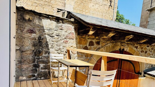 A wooden deck with a table and chairs, a stone wall, and a wooden barrel.