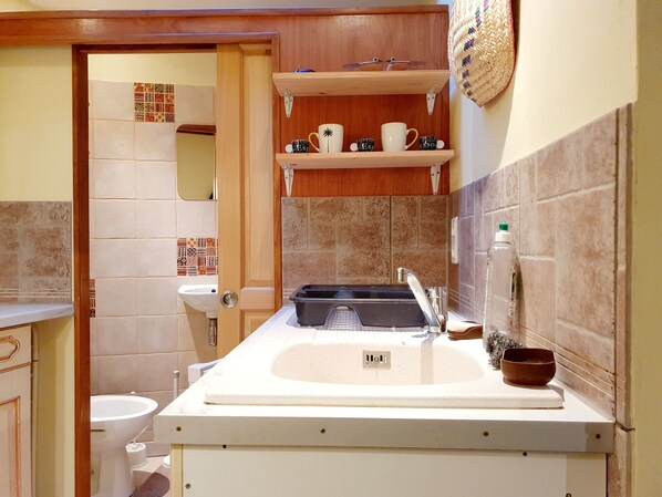 A bathroom with a sink, toilet, and a shelf with coffee cups.